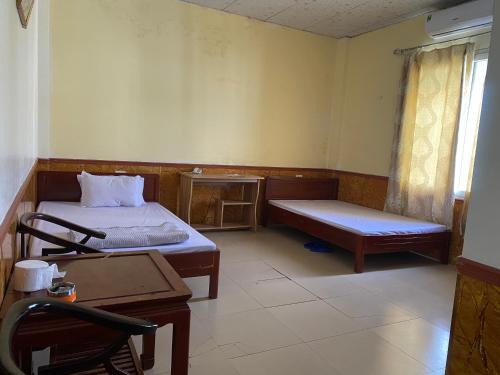 a room with two beds and a bench and a table at Nhà nghỉ FAMY in Móng Cái