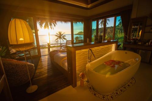 a bathroom with a tub and a bed with a view of the ocean at The Beach Natural Resort Koh Kood in Ko Kood