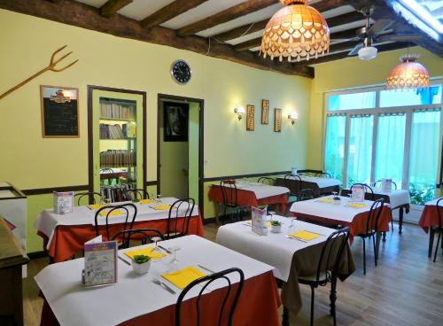 un restaurante con mesas y sillas blancas y ventanas en Hôtel La Fontaine en Lourdes