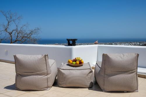 two chairs and a bowl of fruit on a patio at I K I A Since 1980 by Calm Collection in Fira