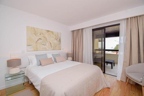 a white bedroom with a large bed and a balcony at Stylish One Bedroom Apartment with Swimming Pool in Cascais
