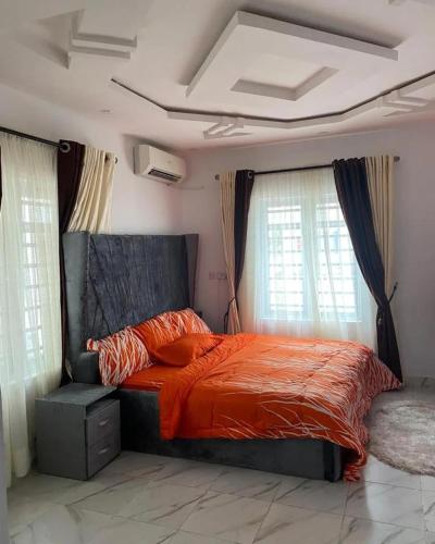 a bedroom with a bed with an orange comforter and windows at Immaculate 2-Bed Apartment in Lekki Ajah in Lekki