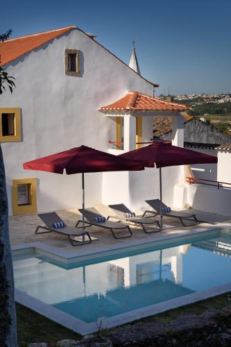 a pool with two umbrellas and chairs next to a house at Casa Lidador - Obidos in Óbidos