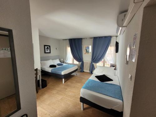 a small room with two beds and blue curtains at Le Cérétan Hôtel in Céret