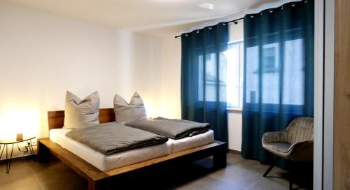 a bedroom with a bed with blue curtains and a chair at Moselufer Apartments in Ürzig