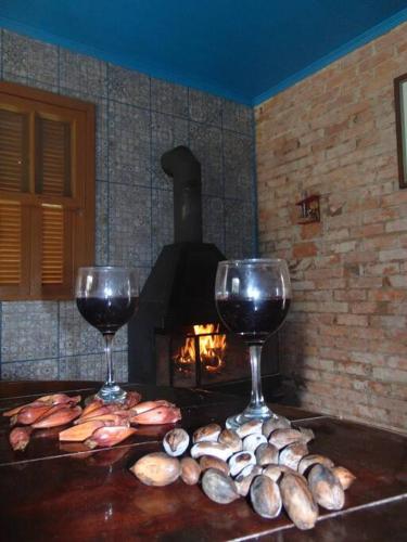 two glasses of wine on a table with a fireplace at Casa de Campo Província Minosso in Farroupilha