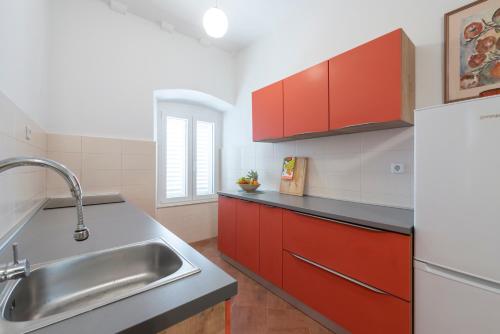 uma cozinha com armários vermelhos e um lavatório de aço inoxidável em Apartment Two Oranges em Dubrovnik