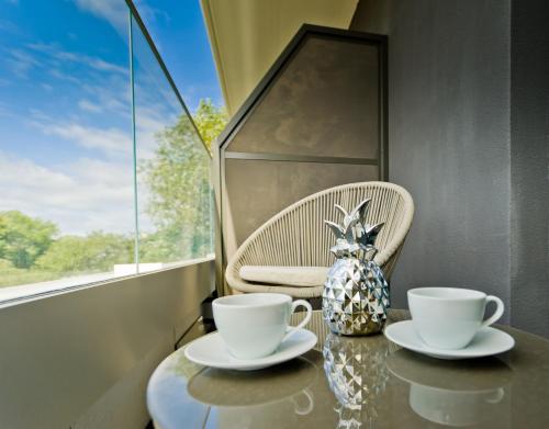 a table with two cups and a vase on it at Unique Baltic Apartments - Apartament z garażem in Kołobrzeg