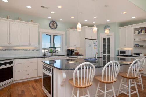a kitchen with white cabinets and a counter with chairs at Turtle Watch Too by Oak Island Accommodations in Caswell Beach