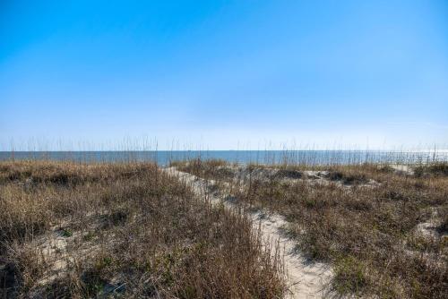 a path through a field with the ocean in the background at Turtle Watch Too by Oak Island Accommodations in Caswell Beach