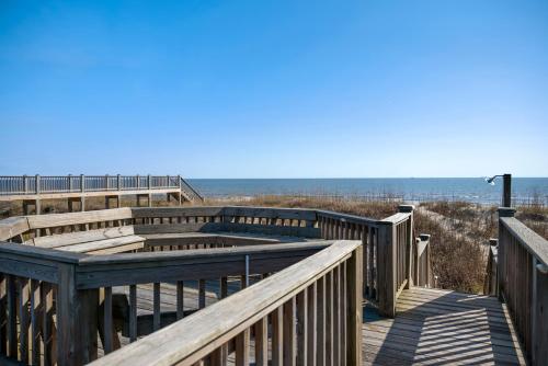 a boardwalk at the beach with the ocean in the background at Turtle Watch Too by Oak Island Accommodations in Caswell Beach