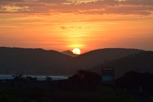 a sunset with the sun setting over a mountain at Marola’s Búzios in Búzios