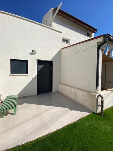 a white building with a door and a green bench at סוויטת הגן השקט- סוויטה מושלמת במעלות in Ma'alot Tarshiha