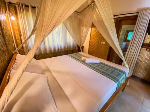 a bed in a room with curtains and a bedvisor at Sayang Mama Inn in Gili Air
