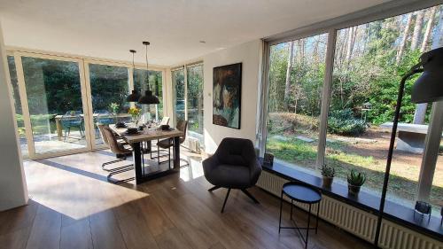 a living room with a table and chairs and windows at Natuurhuis Boscoso met openhaard en elektr.fietsen in Barchem