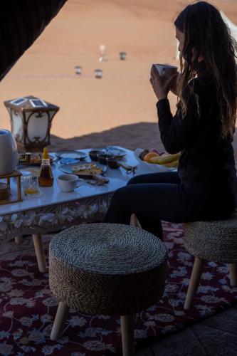 a woman sitting at a table drinking from a cup at Luxury Desert Camp Oman in Al Wāşil