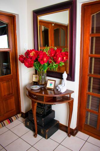 a vase of red flowers on a table with a mirror at Tengo guest house in Phalaborwa