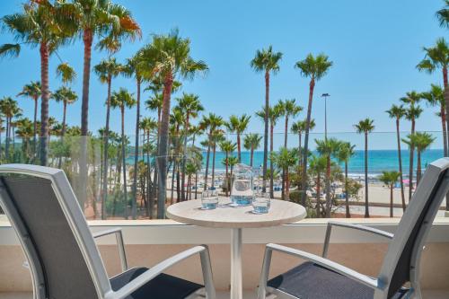 a table and chairs on a balcony with palm trees and the ocean at Hipotels Mediterraneo Club in Sa Coma