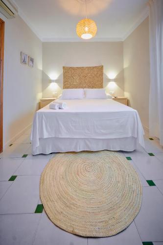 a bedroom with a white bed with a rug on the floor at La Posada Hospedería in Vejer de la Frontera