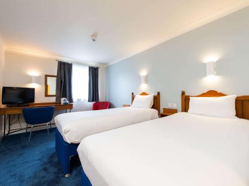 a hotel room with two beds and a desk at ibis budget Glasgow Cumbernauld in Glasgow