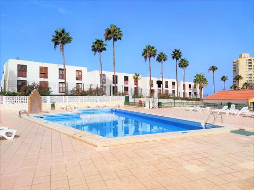 Una piscina con palmeras y un edificio. en Bungalow in Altamar complex, en Arona