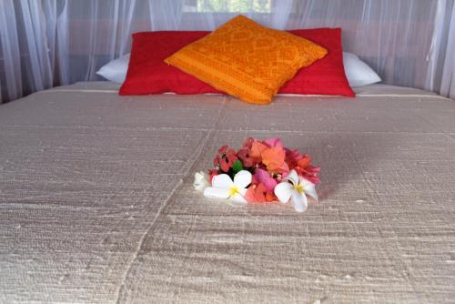 a bouquet of flowers on a bed with red pillows at Rumah Pampa at Pachamama in Nembrala