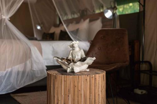 a statue of a monkey sitting on a table next to a bed at Umkumbe Bush Lodge - Luxury Tented Camp in Sabi Sand Game Reserve