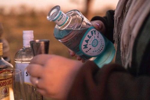 a person is holding a bottle of alcohol at Umkumbe Bush Lodge - Luxury Tented Camp in Sabi Sand Game Reserve