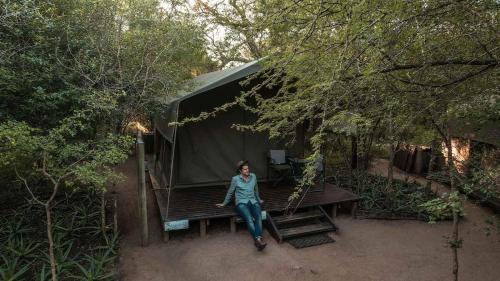 a woman sitting on a picnic table in front of a tent at Umkumbe Bush Lodge - Luxury Tented Camp in Sabi Sand Game Reserve