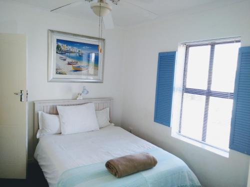 Ce lit se trouve dans une chambre dotée de fenêtres à volets bleus. dans l'établissement Little Greece - Beach House Apartment by Mykonos, à Langebaan