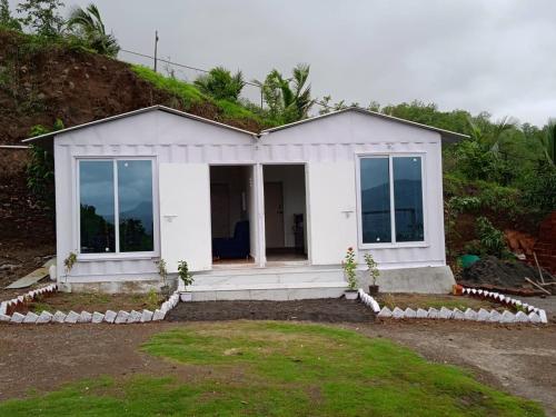 a small white house with glass doors on a hill at Jandyal Farm House in Malshej Ghat