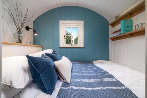 a bedroom with a bed with blue walls and a window at Skylark hut in the Hampshire countryside in Oakley