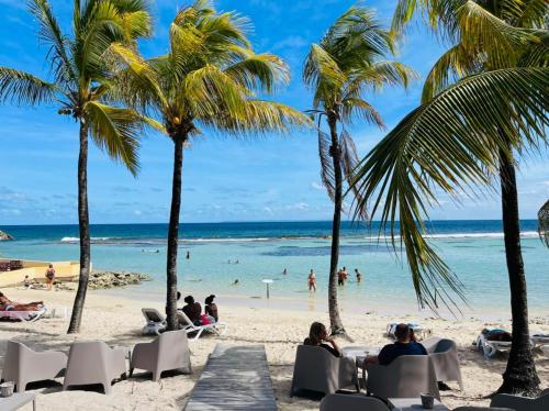 a beach with palm trees and people on the beach at Villa Nomilou Beach avec Accès direct Plage in Saint-François