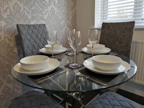 a glass table with plates and wine glasses on it at StayNEC LAMPREY- Lux Apartment - Birmingham - For Company, Contractor & Leisure Stays NEC, HS2, JLR, Airport in Kingshurst