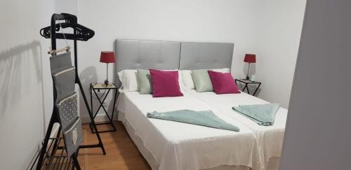 een slaapkamer met een groot wit bed met roze en groene kussens bij Apartamento cerca de la Playa de Las Canteras in Las Palmas de Gran Canaria