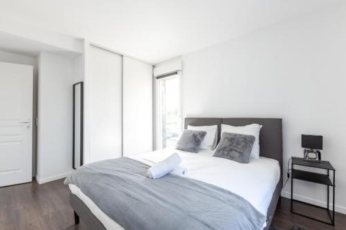a white bedroom with a large bed with two pillows at La Canopée By Plaza in Serris