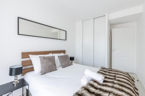 a white bedroom with a bed and a mirror at La Canopée By Plaza in Serris