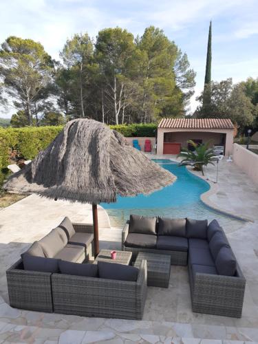 a couch and a straw umbrella next to a pool at La Bastide Des Selves in Draguignan