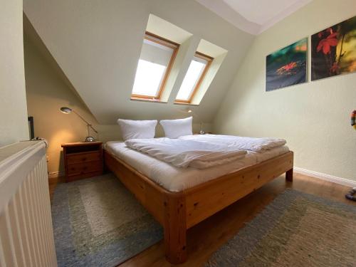 a bedroom with a wooden bed with white sheets and two windows at Haus Jenny, Wohnung E3b, Sonne rundum in Boltenhagen