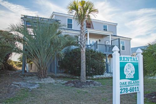 a rental house with a sign in front of it at Fairwinds by Oak Island Accommodations in Caswell Beach