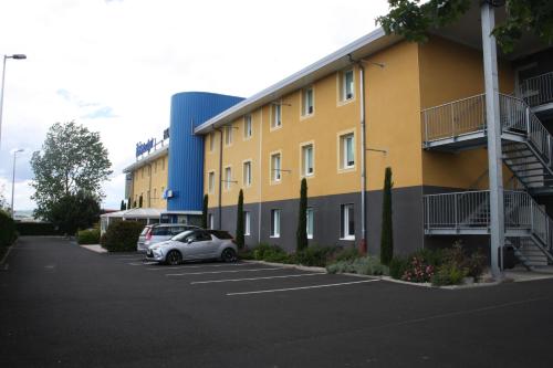 a yellow building with cars parked in a parking lot at ibis budget Issoire in Issoire