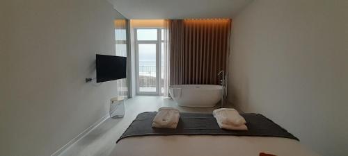 a white bathroom with a tub and a television at Porto Covo Praia Hotel & SPA in Porto Covo