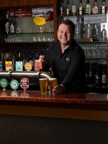 a man standing behind a bar with a glass of beer at The Tanunda Club Guest Suites in Tanunda