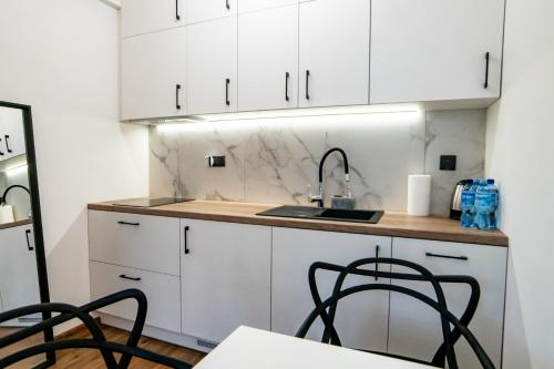 a kitchen with white cabinets and a sink and chairs at Komfortowe studio w centrum miasta nr 1 in Radom