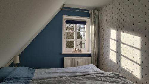 a blue bedroom with a bed and a window at Wohnung Ankerplatz in Wrixum