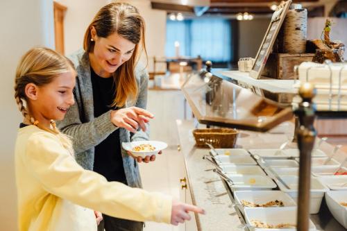 une femme tendant un bol de nourriture à une fille dans l'établissement Hotel Mittagskogel Pitztal, à Sankt Leonhard im Pitztal