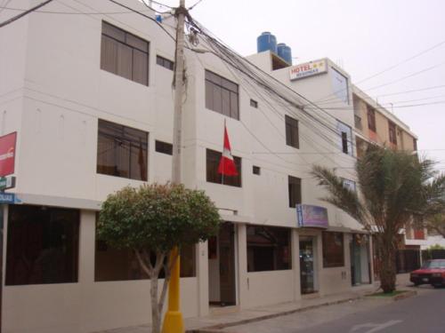 a white building with a red flag in front of it at Hotel Begonias in Lambayeque
