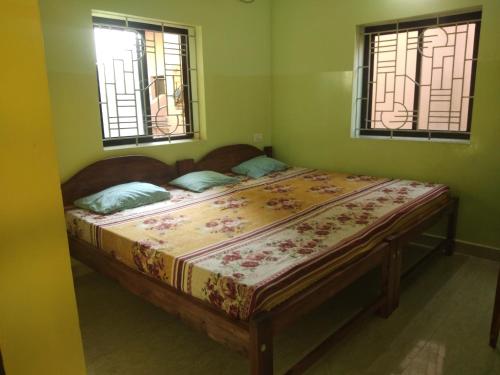 a bed in a room with two windows at Luiza Guest House in Baga