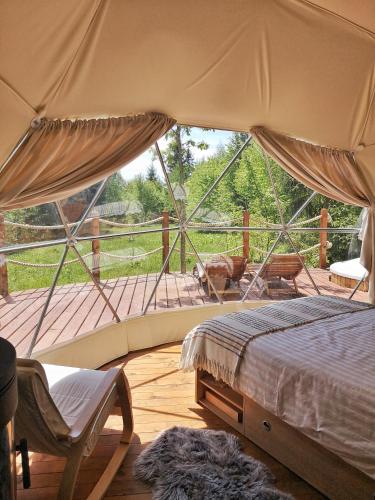 Tienda de campaña con cama y silla en la cubierta en Medve Dome - Luxury Camping in the middle of nature en Vlăhiţa