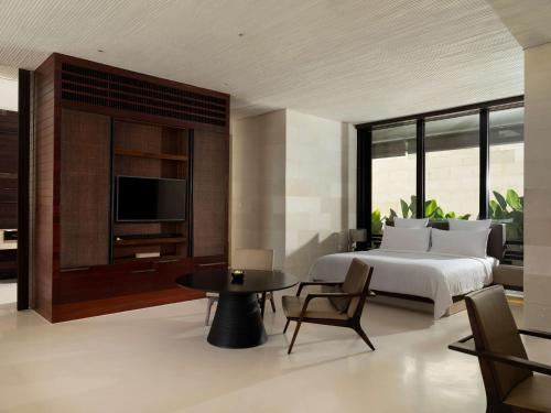 a bedroom with a bed and a tv and a table at Alila Villas Uluwatu in Uluwatu